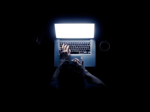 Woman using a laptop computer in darkness with her hands illuminated by the computer screen isolated on black background